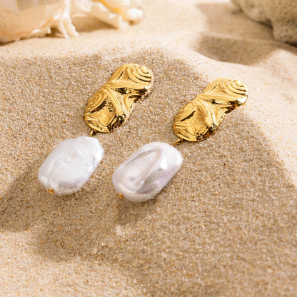 Ein Paar goldener Ohrhänger mit einer organischen, strukturierten oberen Platte und einem tropfenförmigen Süßwasserperlen-Anhänger, gezeigt in der Draufsicht.