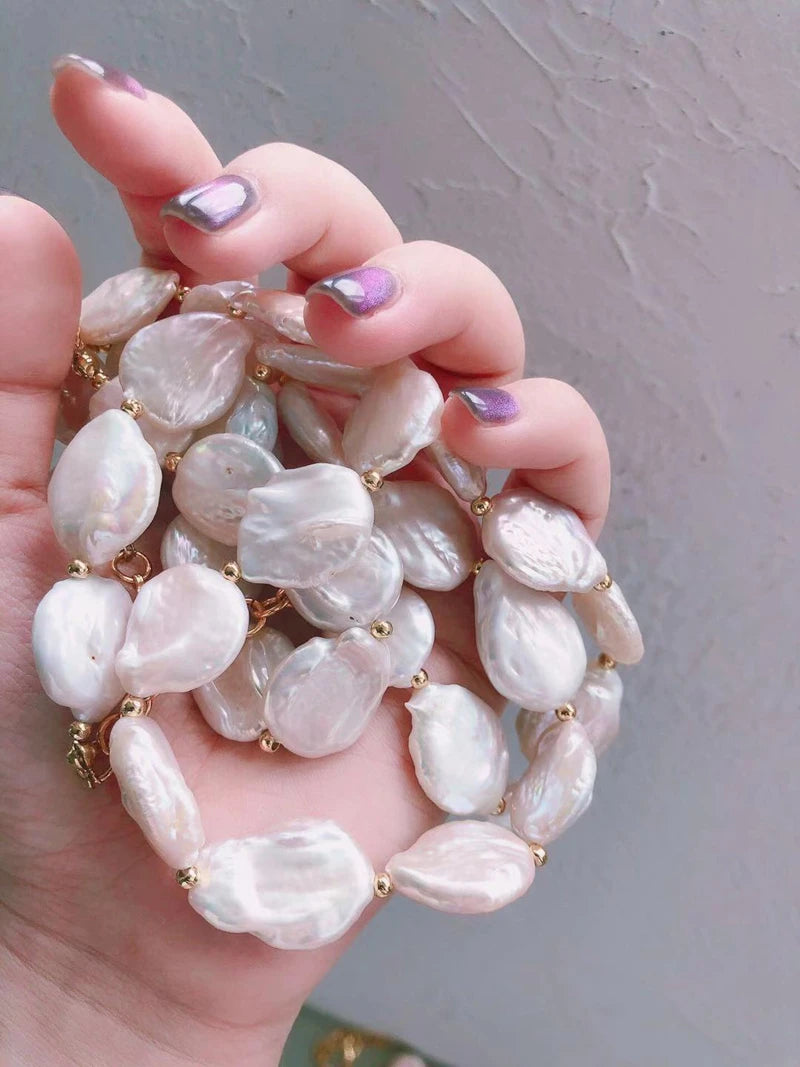 Nahaufnahme einer Hand hält die 18K vergoldete Halskette mit großen, flachen Süßwasserperlen