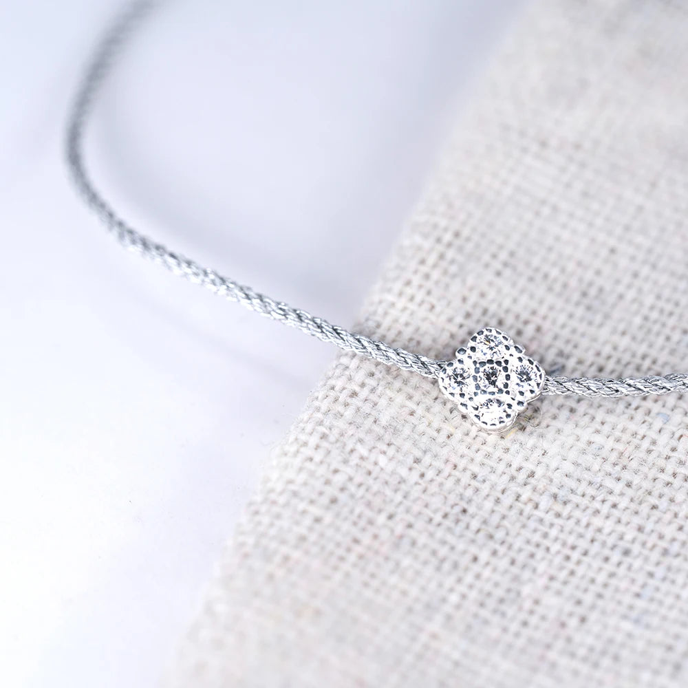 Nahaufnahme eines filigranen Armbands mit einem schimmernden, zentralen Anhänger aus 925er Silber, besetzt mit einem quadratischen Zirkoniastein, liegend auf einem grob gewebten, hellen Stoff.
