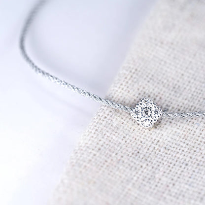 Nahaufnahme eines filigranen Armbands mit einem schimmernden, zentralen Anhänger aus 925er Silber, besetzt mit einem quadratischen Zirkoniastein, liegend auf einem grob gewebten, hellen Stoff.
