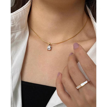 Nahaufnahme einer Frau, die die goldene Kette mit dem rechteckigen Zirkonia-Anhänger trägt; dazu kombiniert sie ein schwarzes Top, eine weiße Bluse und einen passenden Goldring.