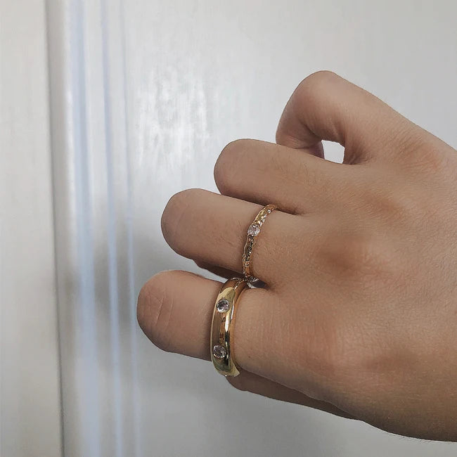 Damenhand mit gestapelten vergoldeten Ringen, darunter der schmale gehammerte Ring mit Zirkonia-Besatz.