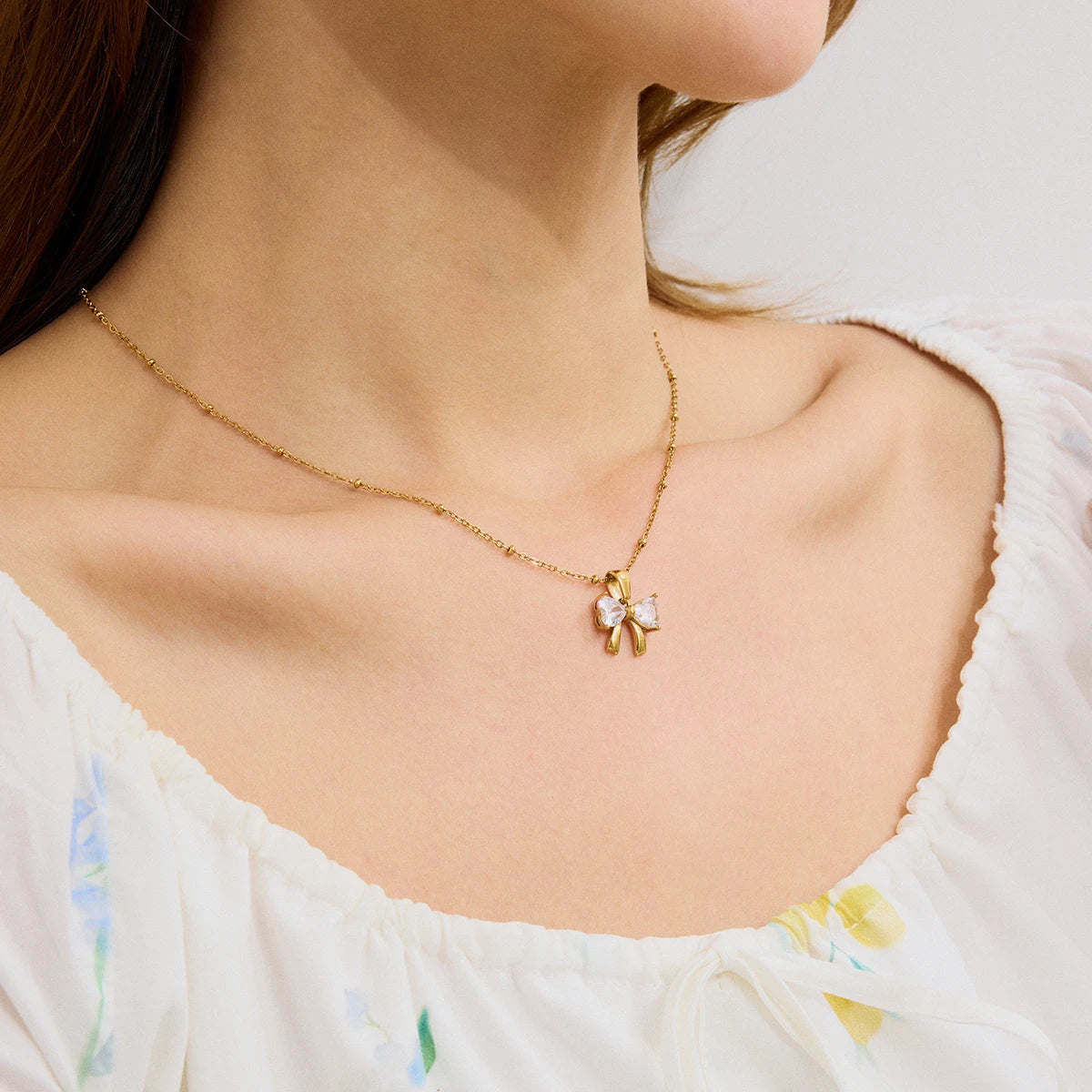 Trageansicht einer filigranen goldene Edelstahlkette mit glitzerndem Schleifen-Anhänger aus Zirkonia an einem Model
