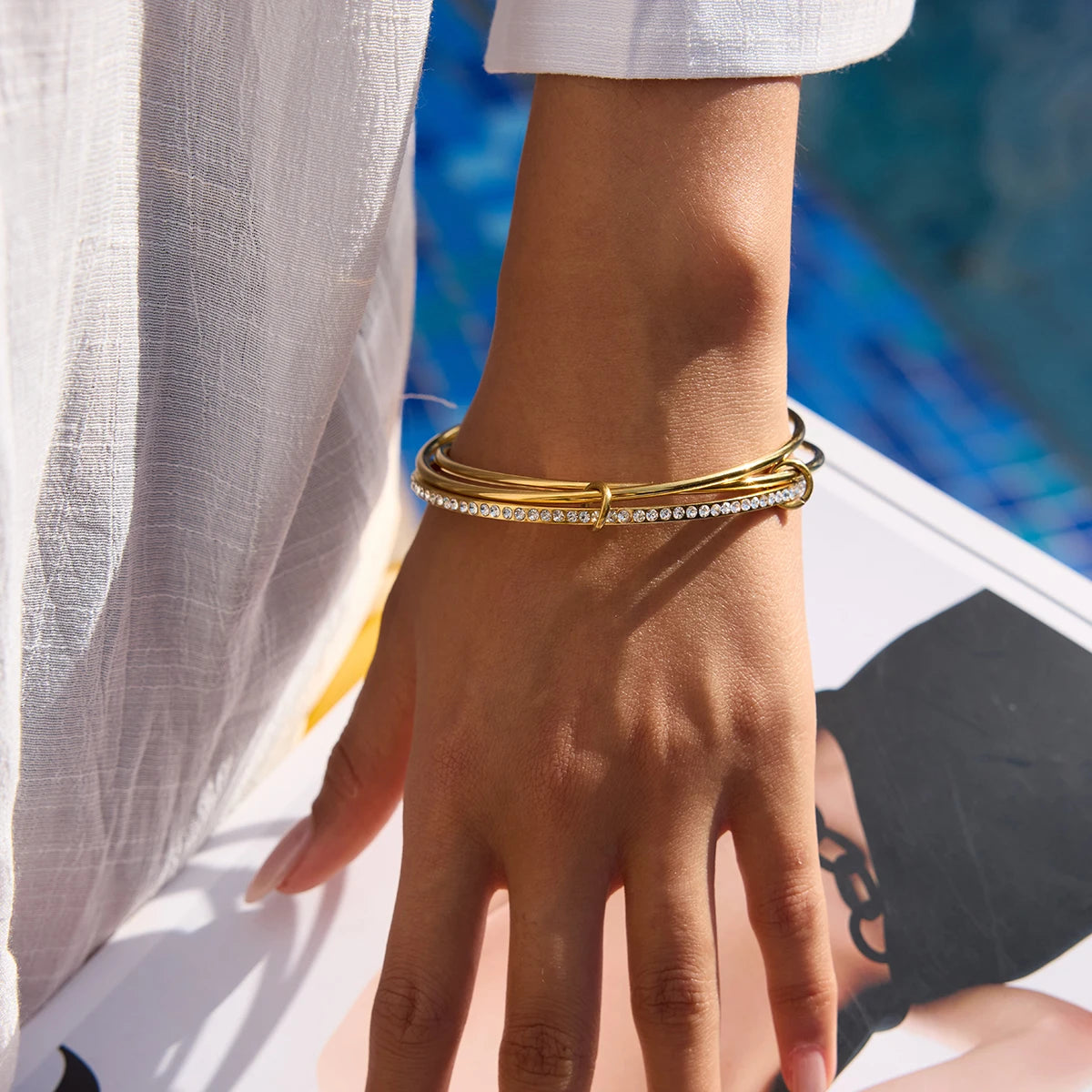 „Modernes Multilayer-Armband in Gold-Optik an einem Handgelenk getragen, kombiniert minimalistisches Design mit glamourösen Akzenten.“