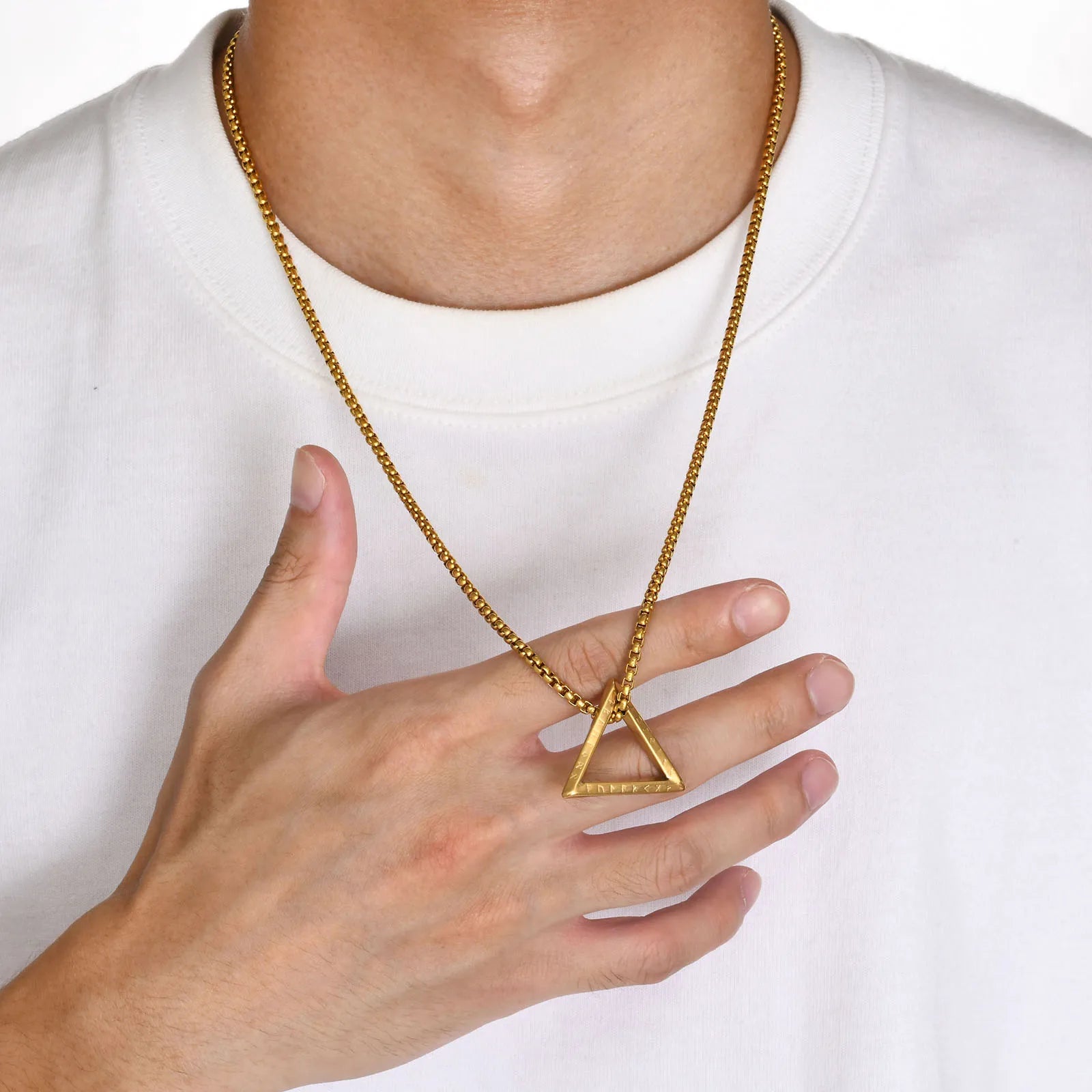 Nahaufnahme eines Mannes, der eine goldfarbene Edelstahlkette mit offenem dreieckigen Anhänger trägt und die Kette mit der Hand berührt, über einem weißen T-Shirt.