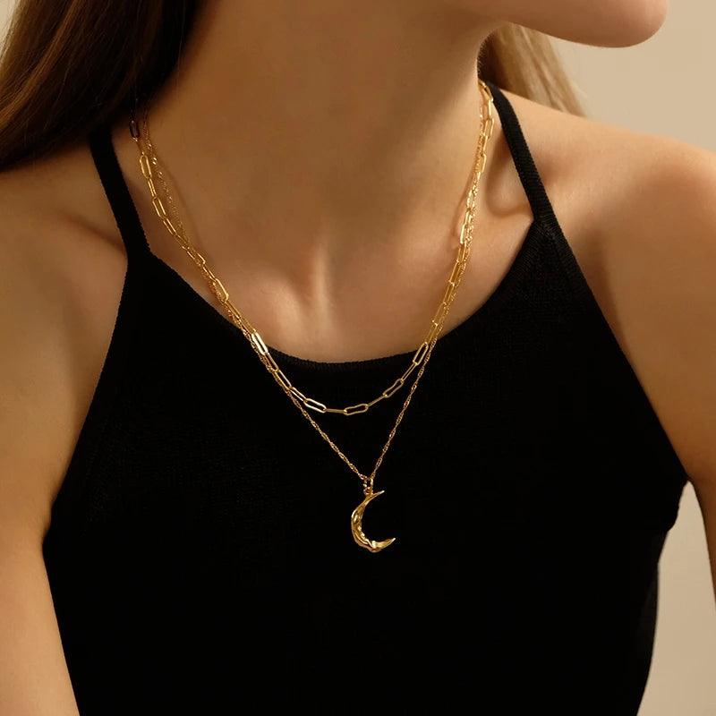 Zweireihige Layering-Halskette aus 18K vergoldetem Messing mit einer Paperclip-Gliederkette und einem Sichelmond-Anhänger an einer Frau im schwarzen Top.