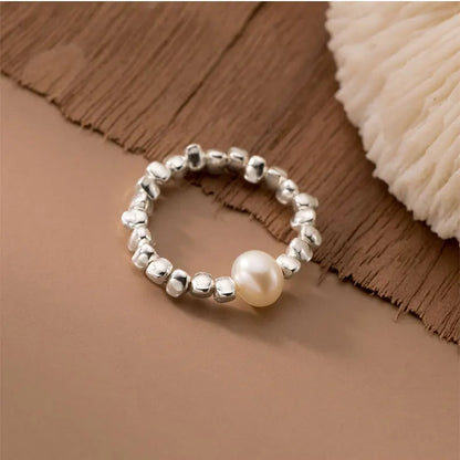 Offener 925 Silber Ring mit unregelmäßiger Oberfläche und einer Acrylperle. Der Ring liegt auf einem braun-beigen Hintergrund.