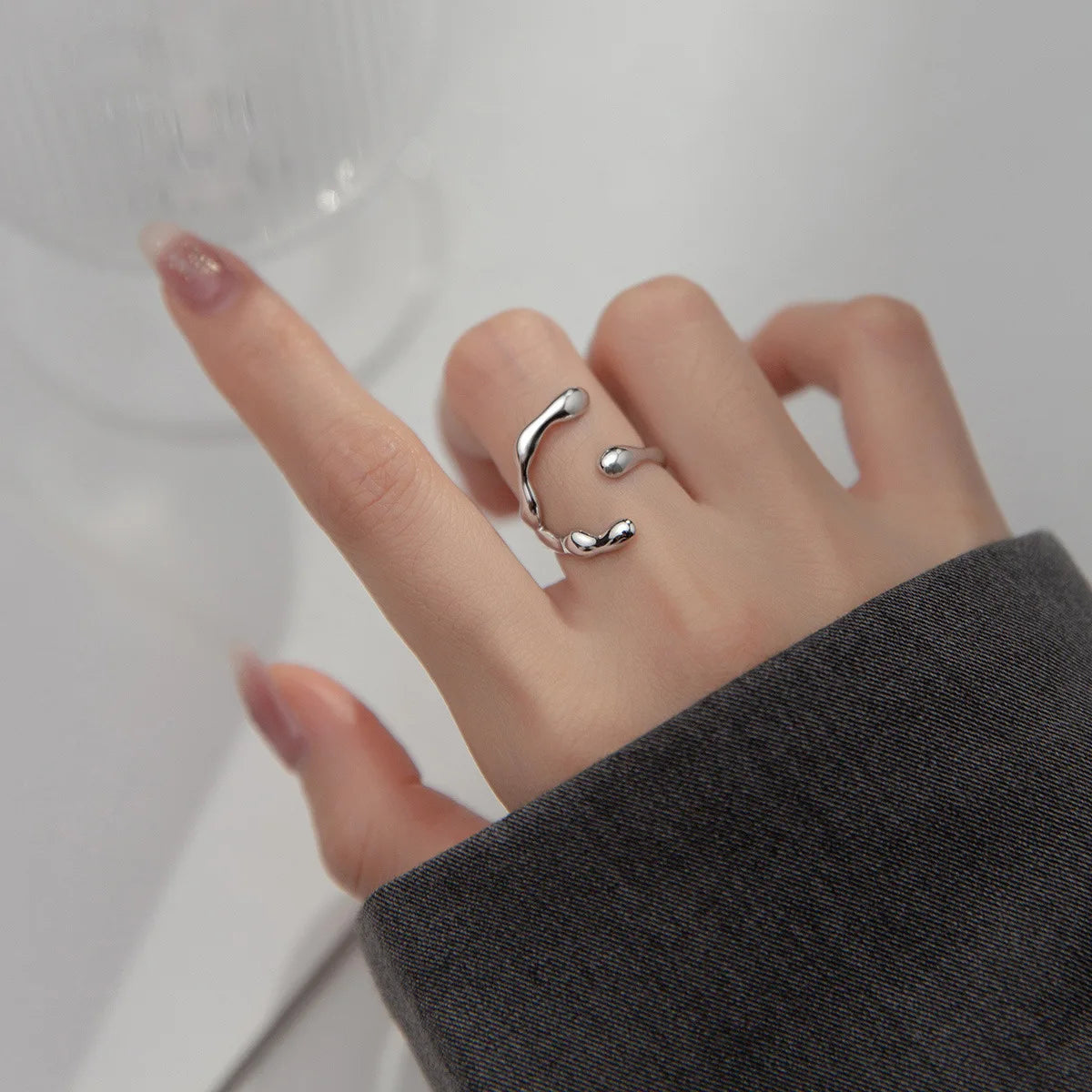 Hand einer Frau, die einen minimalistischen, offenen, doppelten Ring aus 925er Silber trägt, dessen Enden spiralförmig oder C-förmig gebogen sind.