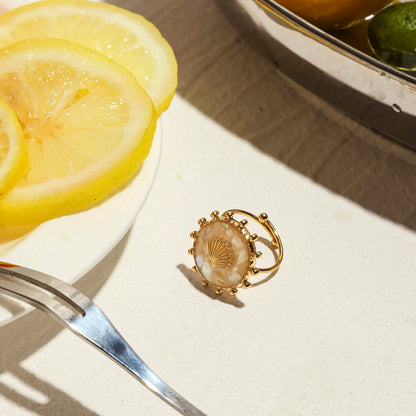 Ein Ring aus 18K vergoldetem Edelstahl mit einem Muschel-Symbol auf einer Gabel, neben einer Zitronenscheibe.