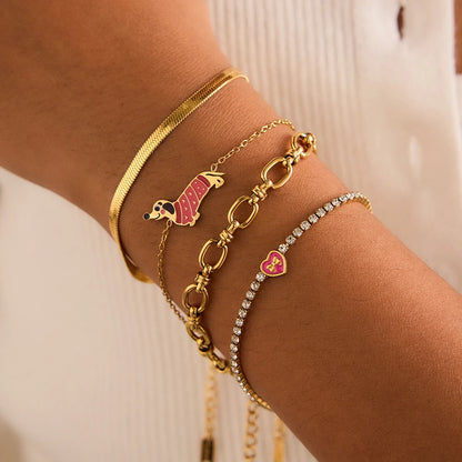 Detailansicht eines Handgelenks mit mehreren geschichteten Armbändern, darunter das goldvergoldete Edelstahl-Armband mit dem rosa Dackel-Anhänger in Kombination mit einem Gliederarmband und einem Schlangenarmband.