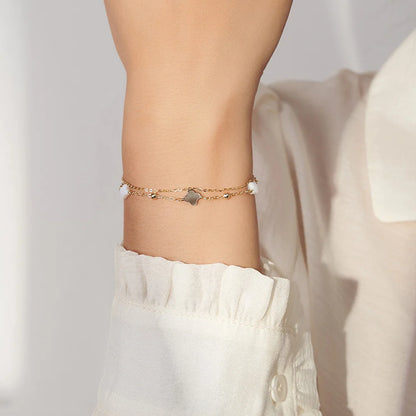 Nahaufnahme: Frau trägt zartes, doppeltes Gold-Armband mit Kleeblättern und Kügelchen am Handgelenk.