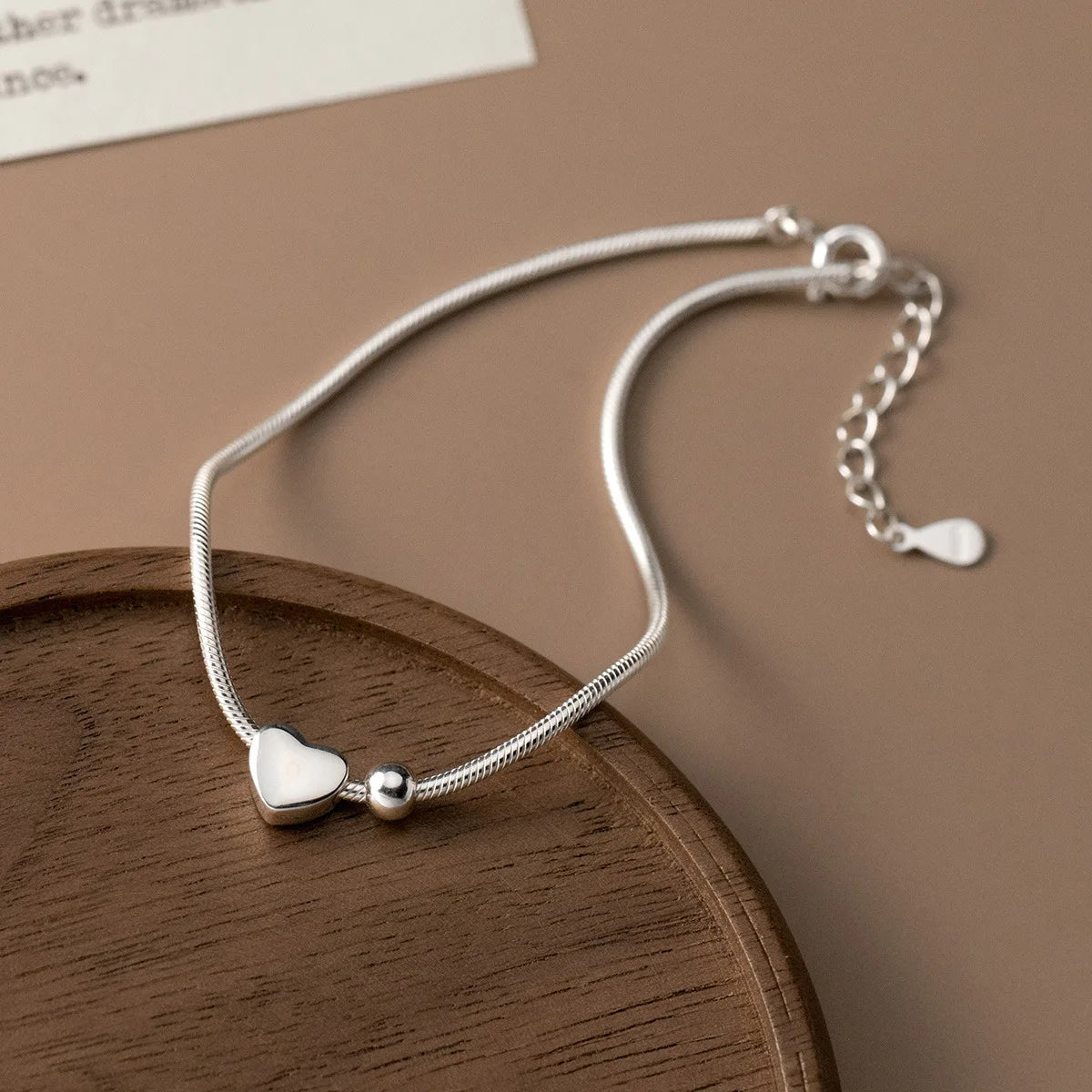 Schlichtes Schlangenarmband aus 925er Silber mit verstellbarer Verlängerungskette und Federringverschluss elegant auf einem Holzschälchen arrangiert