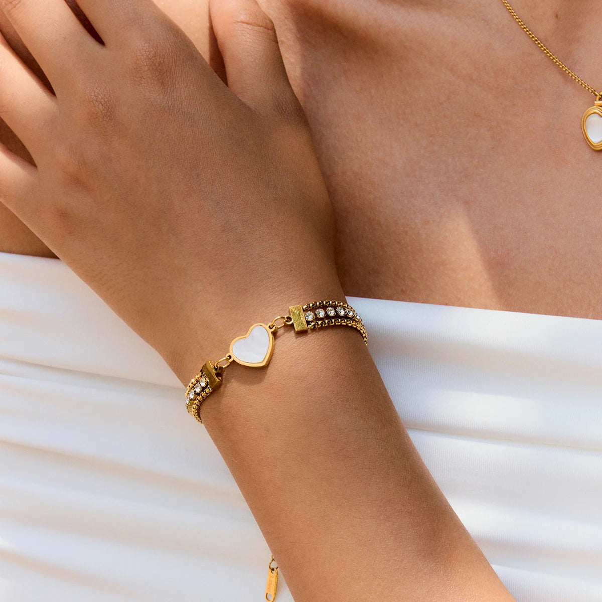 Modell trägt ein mehrreihiges goldenes Herz-Armband aus 18K vergoldetem Edelstahl, besetzt mit einer Reihe funkelnder Zirkonia-Steine und einem zentralen, weiß schimmernden Herz-Inlay.
