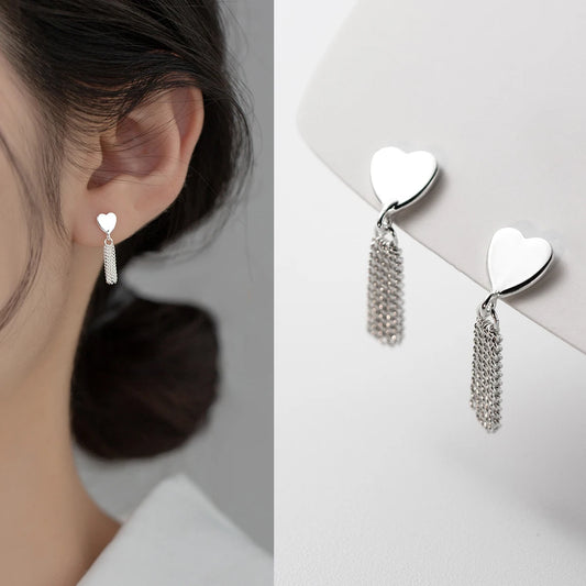 Seitenprofil einer Frau mit hochgestecktem Haar, die einen eleganten Herz-Ohrring aus 925er Sterling Silber mit fein herabhängenden Fransenketten trägt.