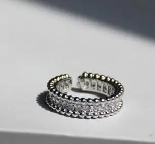 Ein silberfarben glänzender Ring, flach liegend im harten Licht, wodurch die Reflexionen der Zirkonia-Steine und die detailreiche Verarbeitung des Messings besonders scharf hervortreten.
