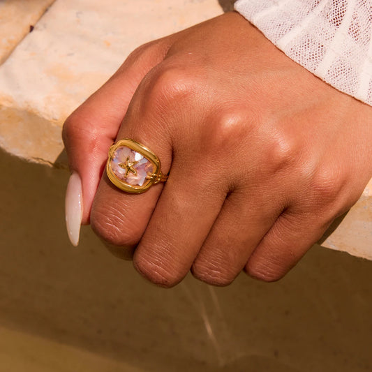 Zwei Ringe aus 18K vergoldetem Edelstahl, darunter der ovale Ring mit roséfarbenem Stein und Seestern-Symbol, am Finger einer Person.