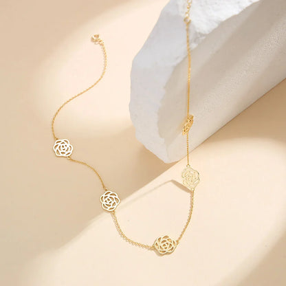 Elegantes Stillleben der filigranen Kette aus 14K Gold mit Rosenblüten-Anhängern auf einem strukturierten, cremefarbenen Hintergrund.