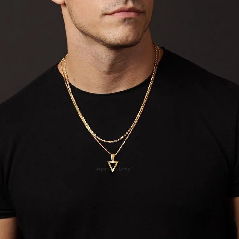 Mann trägt zwei goldfarbene Edelstahl-Halsketten: eine längere mit einem unauffälligen, dreieckigen Anhänger und eine kürzere mit einem schlichten, rechteckigen Anhänger.